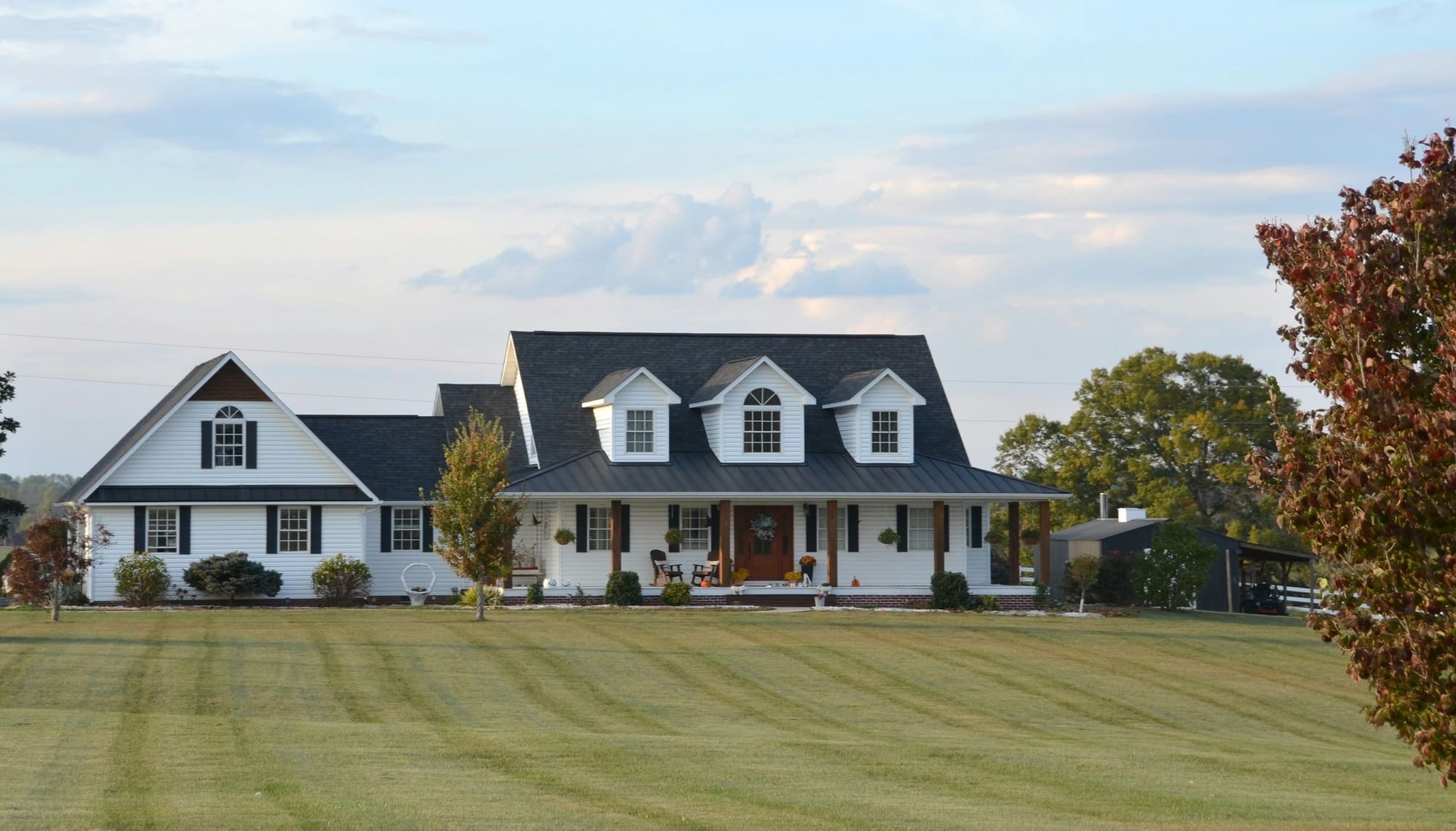 A welcoming white farmhouse with wrap-around porch in autumn